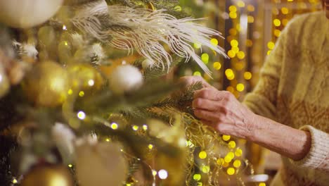 Older-Woman-Approaching-The-Christmas-Tree,-Hangs-Christmas-Decorations