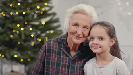 Happy-Grandmother-Talking-To-Her-Granddaughter-While-They-Are-Holding-Their-Gifts-And-Looking-At-Camera-In-Christmas-Morning
