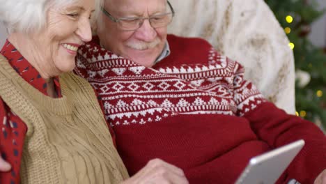 Feliz-Pareja-Mayor-Sentada-En-Un-Sofá-Y-Usando-Una-Tableta-Digital-En-Navidad