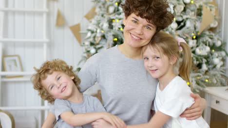 Schöne-Mutter,-Die-Ihre-Kleinen-Kinder-Umarmt-Und-An-Weihnachten-In-Die-Kamera-Lächelt