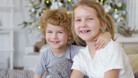 Entzückender-Kleiner-Junge-Und-Seine-Süße-Schwester-Lächeln-An-Weihnachten-Zu-Hause-In-Die-Kamera