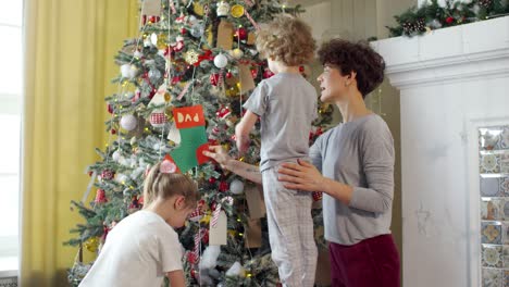 Liebevolle-Mutter-Und-Ihre-Kinder-Schmücken-Gemeinsam-Den-Weihnachtsbaum-In-Einem-Gemütlichen-Wohnzimmer