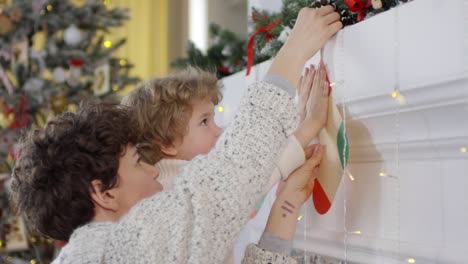 Mutter-Und-Kleiner-Sohn-Hängen-Papierweihnachtsstrümpfe-An-Einem-Kamin-Auf