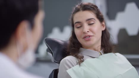 Female-Patient-Sitting-On-Dental-Chair-Talking-To-Unrecognizable-Dentist