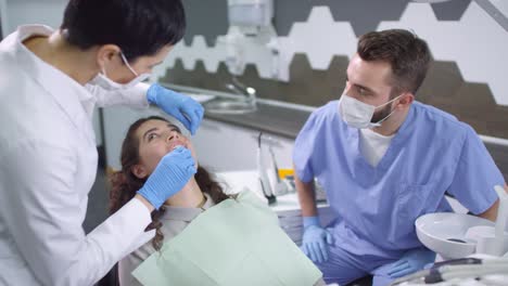 Female-Dentist-Using-Dental-Scaler-And-Tooth-Mirror-Examining-Female-Patient-With-The-Help-Of-Her-Assistant
