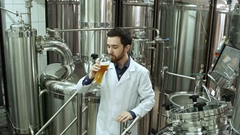 Professioneller-Brauereiangestellter-Im-Laborkittel,-Der-Glas-Untersucht-Und-Frisch-Gebrautes-Bier-In-Der-Brauerei-Probiert