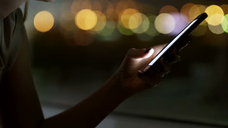 Nahaufnahme-Einer-Frau,-Die-Bei-Dunkelheit-Eine-Nachricht-Auf-Dem-Smartphone-Eingibt,-Mit-Defokussierten-Lichtern-Im-Hintergrund