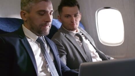 Businessmen-In-Suits-Talking-And-Working-On-Laptop,-Then-Shaking-Hands-And-Making-Deal-While-Traveling-By-Plane