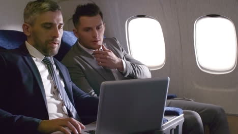 Businessmen-In-Suits-Talking-And-Working-On-Laptop,-Then-Shaking-Hands-And-Making-Deal-While-Traveling-By-Plane-1
