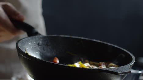 Close-Up-Of-Chef-Hand-Holding-Hot-Pan-And-Adding-Salt-To-It-With-Other-Hand