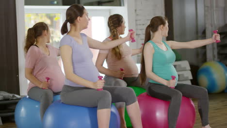 Group-Of-Four-Fit-Pregnant-Women-Training-With-Dumbbells-While-Sitting-On-Stability-Balls-In-Fitness-Class