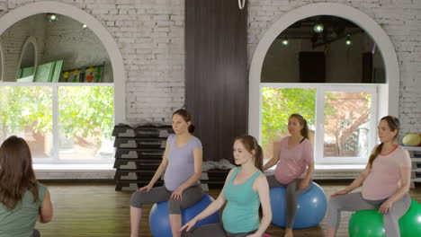Group-Of-Four-Active-Pregnant-Women-And-Their-Female-Fitness-Trainer-Sitting-On-Stability-Balls-In-Gym-And-Doing-Side-Stretching-And-Torso-Rotations-Exercises