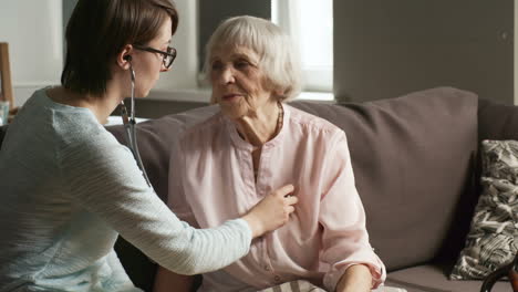 Young-Woman-Using-Stethoscope-And-Listening-To-Heartbeat-Of-Senior-Woman-When-Volunteering-In-Social-Care