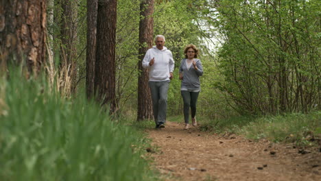 Ground-Level-View-Of-Senior-Man-And-Woman-Running-Along-Forest-Trail