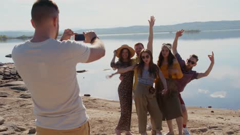 Gruppe-Glücklicher-Junger-Menschen,-Die-Am-Friedlichen-See-Auf-Sand-Stehen-Und-Gemeinsam-Für-Ein-Foto-Posieren