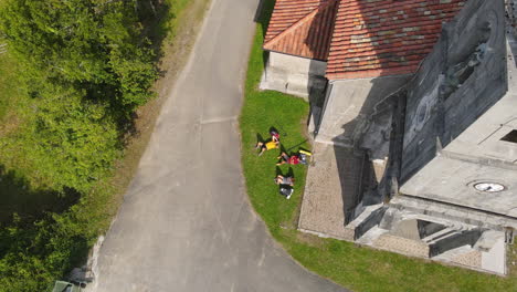 Luftaufnahme-Von-Drei-Rucksacktouristen,-Die-Sich-Auf-Gras-In-Der-Nähe-Einer-Alten-Kirche-Ausruhen