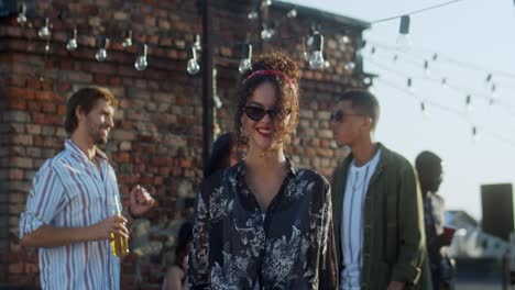 Young-Good-Looking-And-Stylish-Curly-Girl-In-Black-Sunglasses-Posing-And-Smiling-To-The-Camera-At-The-Rooftop-Party