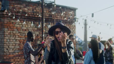 Young-Stylish-And-Beautiful-Girl-In-Black-Sunglasses-And-Hat-Dancing-Cheerfully-In-Front-Of-The-Camera-At-The-Rooftop-Party-At-Daytime
