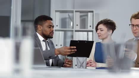 Consultor-Financiero-Masculino-Explicando-El-Plan-De-Negocios-A-Los-Clientes-En-La-Oficina
