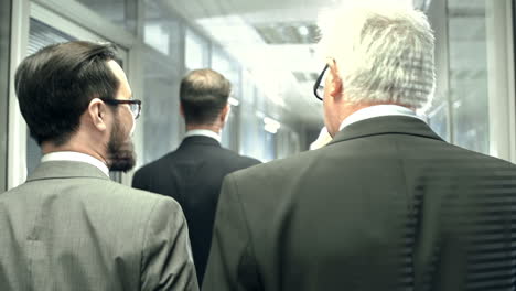 Bearded-Businessman-Walks-Through-A-Hallway-Together-With-An-Older-Gray-Haired-Colleague