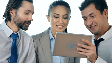 A-Work-Team-Consisting-Of-Two-Men-And-A-Woman-Make-A-Videocall-With-A-Tablet