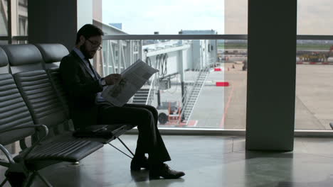 Der-Bärtige-Geschäftsmann-Liest-Eine-Zeitung,-Während-Er-Am-Flughafen-Sitzt-Und-Auf-Den-Abflug-Seines-Fluges-Wartet