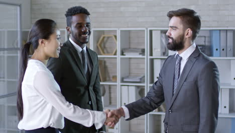 Medium-Shot-Of-Young-Bearded-Businessman-In-Suit-Approaching-Two-Colleagues-And-Shaking-Hands-With-Them-In-Office