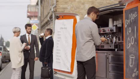 Male-Barista-Working-On-Coffee-Machine-In-Mobile-Van,-And-Group-Of-Multiethnic-Office-Workers-In-Business-Suits-Standing-In-City-Street,-Drinking-From-Disposable-Cups-And-Talking