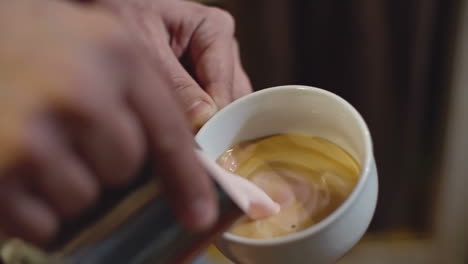 Nahaufnahme-Der-Hände-Von-Barista,-Die-Erdbeerdampfmilch-Aus-Edelstahlkrug-In-Eine-Tasse-Espresso-In-Herzform-Gießen,-Um-Latte-Art-Zu-Machen,-Zeitlupenaufnahme