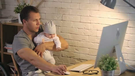 Young-Father-Holding-His-Baby-While-Working-On-The-Computer-At-Home