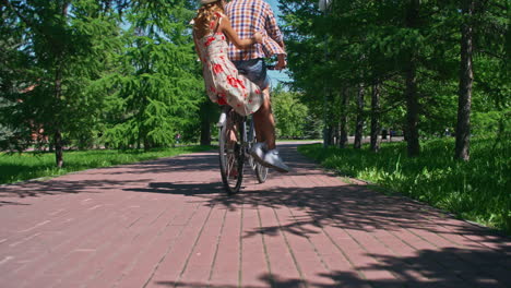 Following-A-Couple-Riding-A-Bike-Through-A-Park-In-Summertime