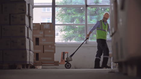 Worker-In-Helmet-And-Yellow-Vest-Pulling-A-Forklift-Loaded-With-Boxes