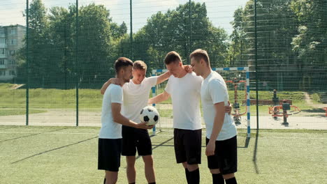 Happy-Young-Street-Soccer-Players-With-Ball-Standing-In-Circle-And-Embracing-On-The-Pitch-Before-Football-Game