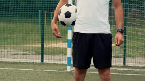 Close-Up-Of-An-Unrecognizable-Football-Player-Standing-And-Holding-Soccer-Ball-On-A-Street-Football-Pitch-1
