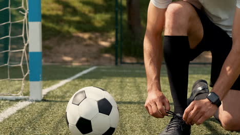 Close-Up-Of-An-Unrecognizable-Football-Player-Tying-His-Soccer-Shoes-On-A-Street-Football-Pitch-1