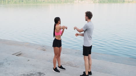 Sportive-Couple-Warming-Up-And-Stretching-Arms-Near-The-River
