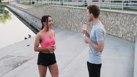Happy-Sportive-Couple-Drinking-Water-And-Talking-To-Each-Other-While-Taking-A-Break-During-Their-Running-Session-In-The-City-1