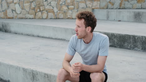 Sportive-Young-Man-Sitting-On-Stairs-And-Drinking-Water-After-Running-Training-Session-In-The-City