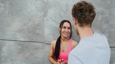 Beautiful-Smiling-Runner-Girl-Leaning-Against-A-Wall-And-Talking-To-Her-Boyfriend-Standing-In-Front-Of-Her-While-They-Are-Taking-A-Break-During-A-Training-Session-In-The-City