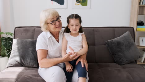 Happy-Grandmother-With-Her-Pretty-Little-Granddaughter-Sitting-On-Her-Knees-On-Sofa-Greeting-And-Talking-On-Video-Call-1