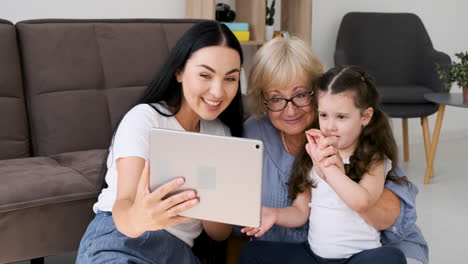 Großmutter,-Mutter-Und-Kleines-Mädchen-Haben-Einen-Videoanruf-über-Ein-Tablet,-Das-Zu-Hause-Auf-Dem-Boden-Sitzt