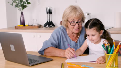 Großmutter-Und-Enkelin-Zeichnen-Am-Tisch-In-Der-Küche-Sitzend,-Während-Sie-Einen-Videoanruf-Auf-Einem-Modernen-Laptop-Führen