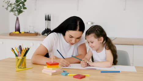 Beautiful-Mom-And-Her-Pretty-Daughter-Sitting-At-Table-In-Kitchen-And-Drawing-Together