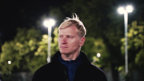 Portrait-Of-Sportive-Blond-Man-Stretching-Neck-Before-Training-In-The-Park-At-Night