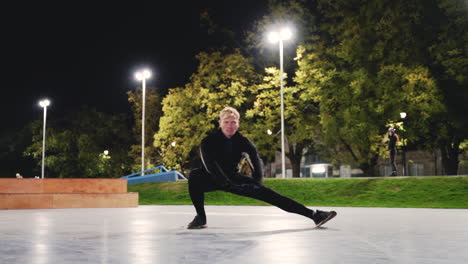 Sportive-Blond-Man-Stretching-Legs-Before-Training-In-The-Park-At-Night