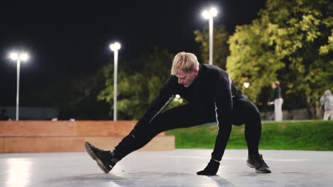 Sportive-Blond-Man-Stretching-Legs-Before-Training-In-The-Park-At-Night-1