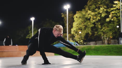 Sportive-Blond-Man-Stretching-Legs-Before-Training-In-The-Park-At-Night-2