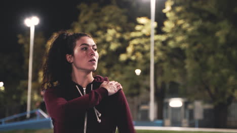 Sportive-Curly-Girl-Stretching-And-Rotating-Arms-In-The-Park-At-Night-1