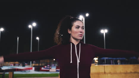Sportive-Curly-Girl-Stretching-And-Rotating-Arms-In-The-Park-At-Night-2