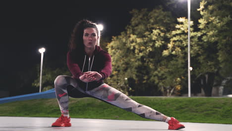 Sportive-Curly-Girl-Stretching-Legs-And-Doing-Side-Lunges-In-The-Park-At-Night